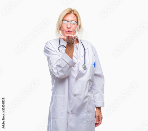 Middle age blonde doctor woman over isolated background looking at the camera blowing a kiss with hand on air being lovely and sexy. Love expression.