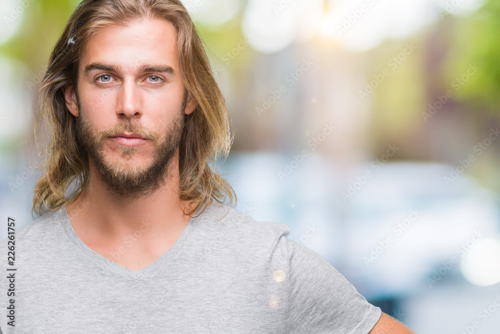 Young handsome man with long hair over isolated background holding football ball with a confident expression on smart face thinking serious Young handsome man with long hair over isolated background holding football ball with a confident expression on smart face thinking serious