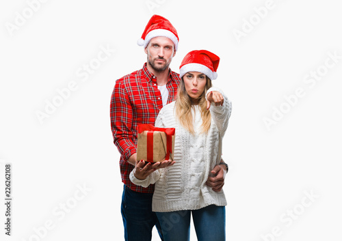 Young couple in love wearing christmas hat and holding present over isolated background pointing with finger to the camera and to you, hand sign, positive and confident gesture from the front