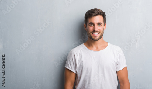 Handsome young man over grey grunge wall with a happy and cool smile on face. Lucky person. photo