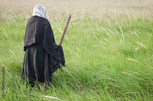 Valokuva evil old witch hunched over the field among the tall grasses, taking a broom