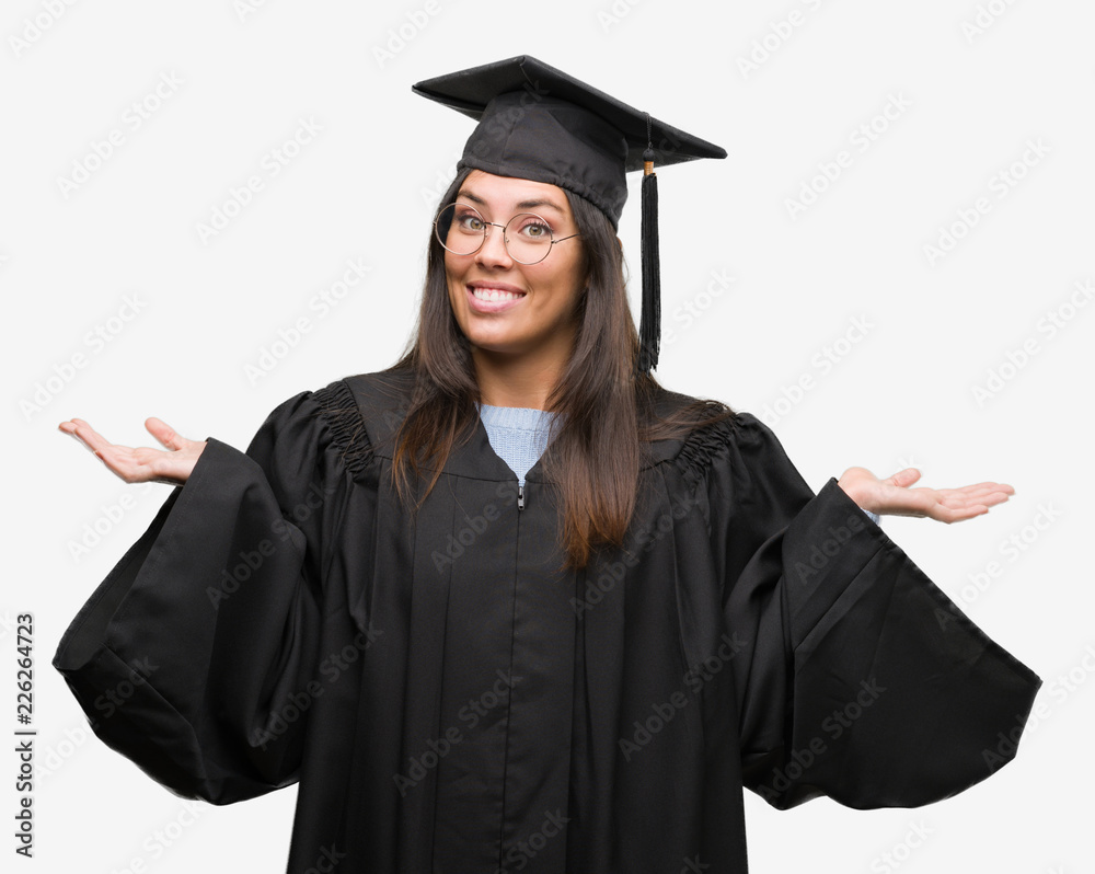 Young hispanic woman wearing graduated cap and uniform clueless and confused expression with arms and hands raised. Doubt concept. Young hispanic woman wearing graduated cap and uniform clueless and confused expression with arms and hands raised. Doubt concept.
