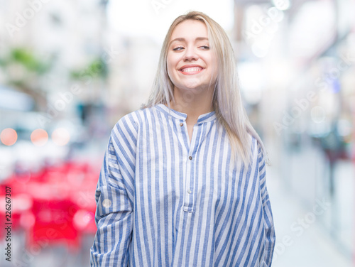 Young blonde woman over isolated background looking away to side with smile on face, natural expression. Laughing confident.