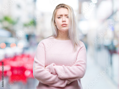 Young blonde woman wearing winter sweater over isolated background skeptic and nervous, disapproving expression on face with crossed arms. Negative person.