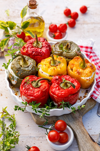 Baked bell peppers stuffed. Mushroom, reis, cheese and herbs stuffed peppers in a baking dish on a white wooden table. A healthy and delicious vegetarian dish.