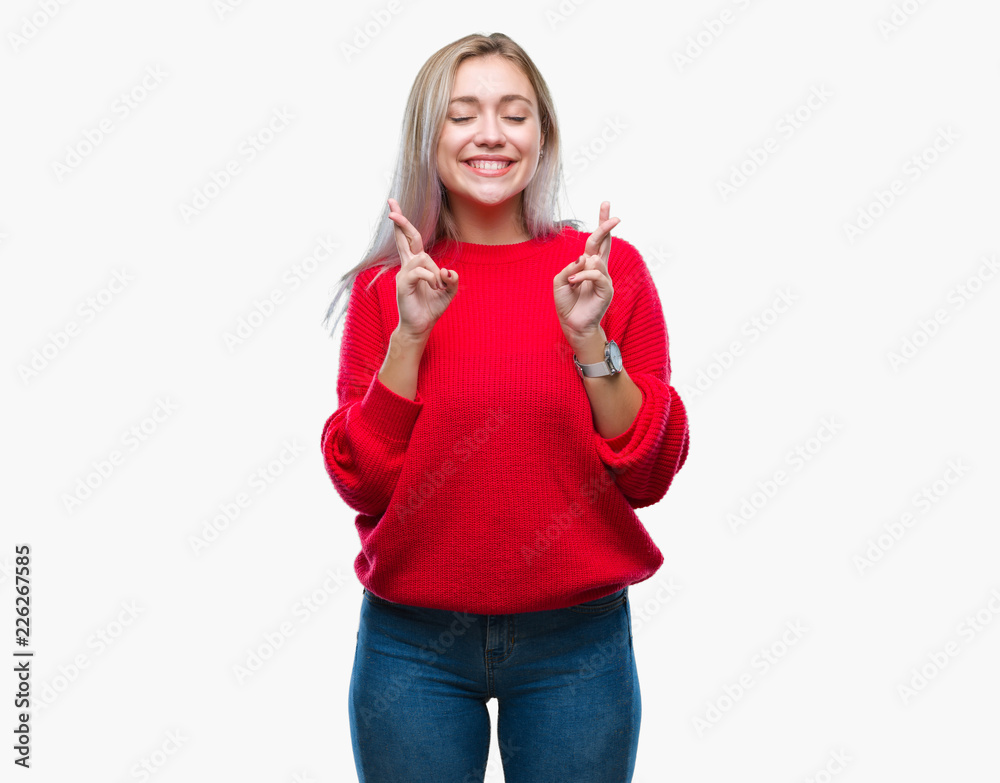 Young blonde woman wearing winter sweater over isolated background smiling crossing fingers with hope and eyes closed. Luck and superstitious concept. Young blonde woman wearing winter sweater over isolated background smiling crossing fingers with hope and eyes closed. Luck and superstitious concept.