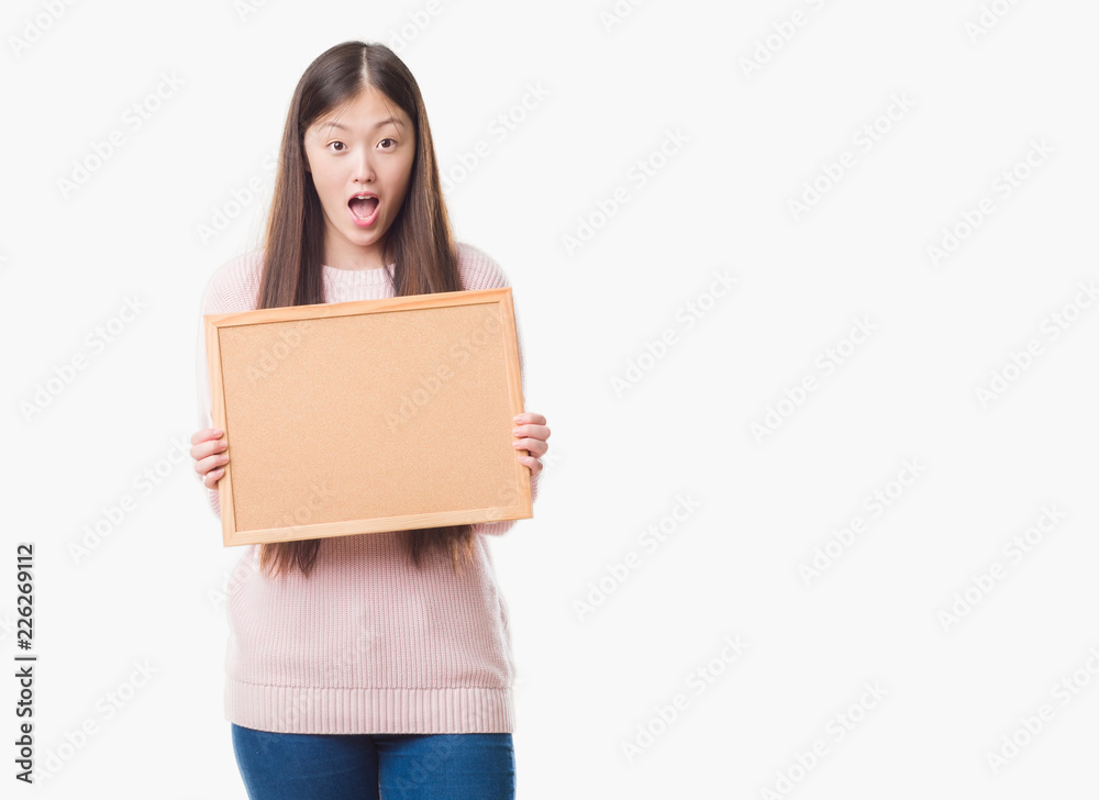Young Chinese woman over isolated background holding corkboard scared in shock with a surprise face, afraid and excited with fear expression Young Chinese woman over isolated background holding corkboard scared in shock with a surprise face, afraid and excited with fear expression