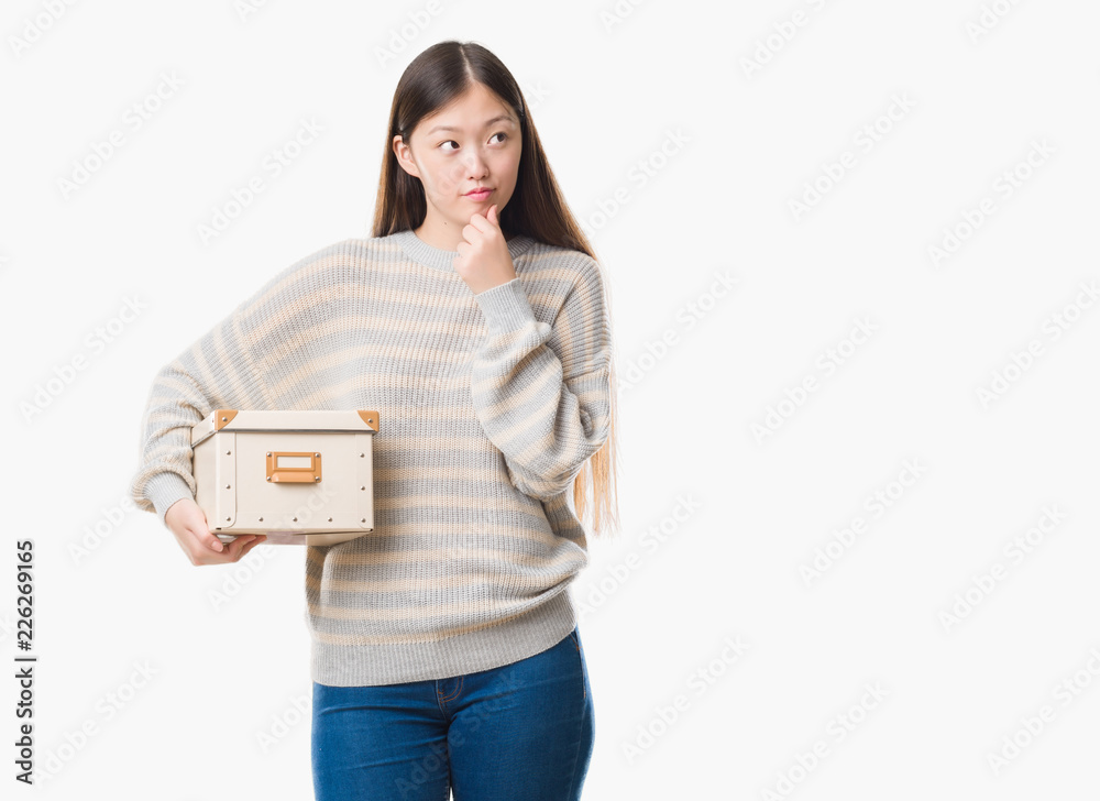 Young Chinese woman over isolated background holding a box serious face thinking about question, very confused idea Young Chinese woman over isolated background holding a box serious face thinking about question, very confused idea