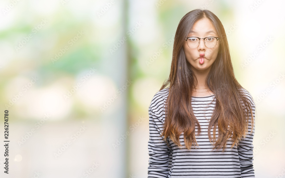 Young asian woman wearing glasses over isolated background making fish face with lips, crazy and comical gesture. Funny expression.
