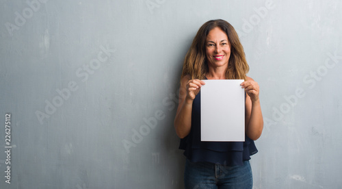 Middle age hispanic woman holding bank paper sheet with a happy face standing and smiling with a confident smile showing teeth