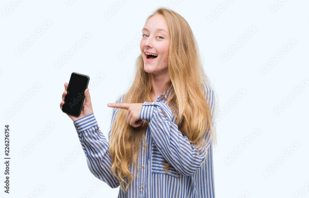 Blonde teenager woman using smartphone very happy pointing with hand and finger Blonde teenager woman using smartphone very happy pointing with hand and finger