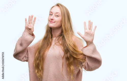 Blonde teenager woman wearing pink sweater showing and pointing up with fingers number nine while smiling confident and happy.