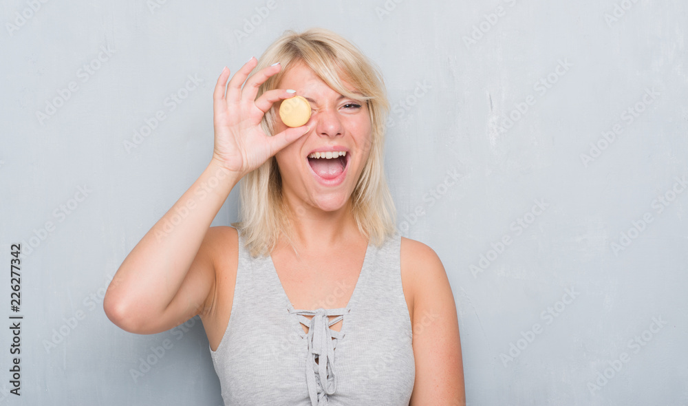 Adult caucasian woman over grunge grey wall eating macaron with a happy face standing and smiling with a confident smile showing teeth