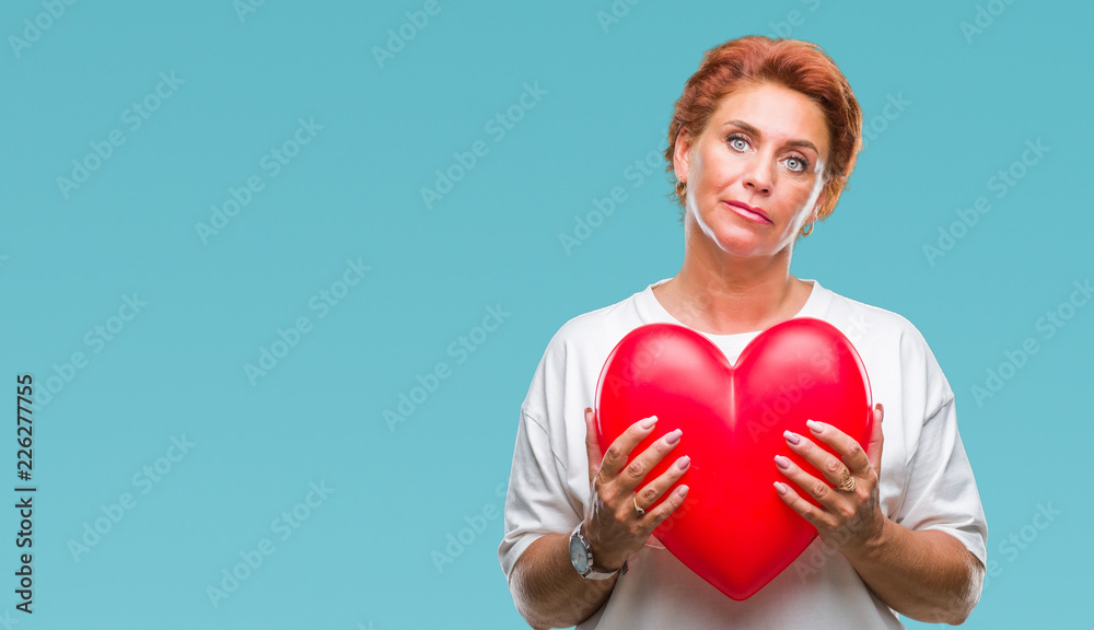 Senior caucasian woman holding red heart in love over isolated background with a confident expression on smart face thinking serious Senior caucasian woman holding red heart in love over isolated background with a confident expression on smart face thinking serious