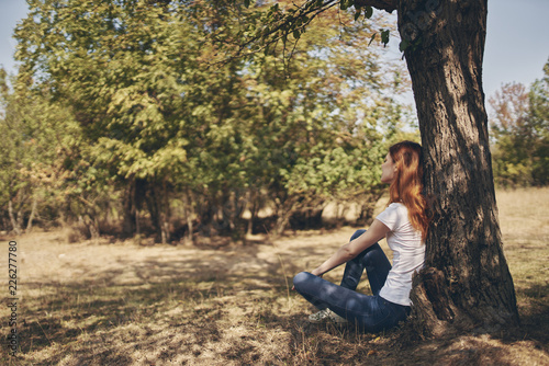 woman sitting on the ground leaning on a tree