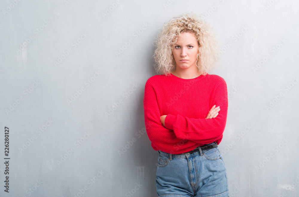 Young blonde woman with curly hair over grunge grey background skeptic and nervous, disapproving expression on face with crossed arms. Negative person. Young blonde woman with curly hair over grunge grey background skeptic and nervous, disapproving expression on face with crossed arms. Negative person.