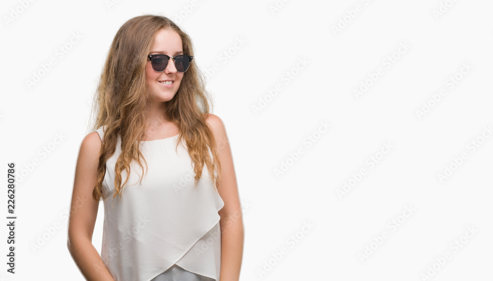Young blonde woman wearing sunglasses looking away to side with smile on face, natural expression. Laughing confident. Young blonde woman wearing sunglasses looking away to side with smile on face, natural expression. Laughing confident.