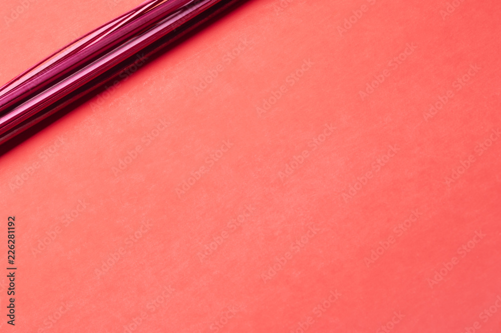 Fototapeta premium A bunch of straight red-painted wood sticks serves as a focal point on a predominantly empty slightly gradient and subtly textured red paper background.