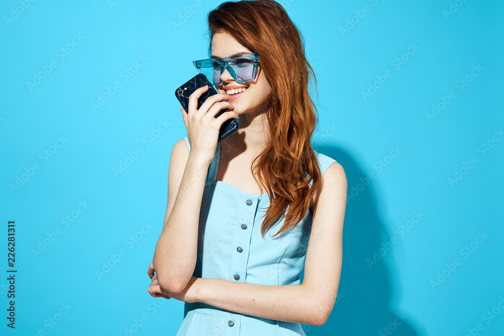 woman in blue glasses and blue dress is holding a phone in her hand woman in blue glasses and blue dress is holding a phone in her hand