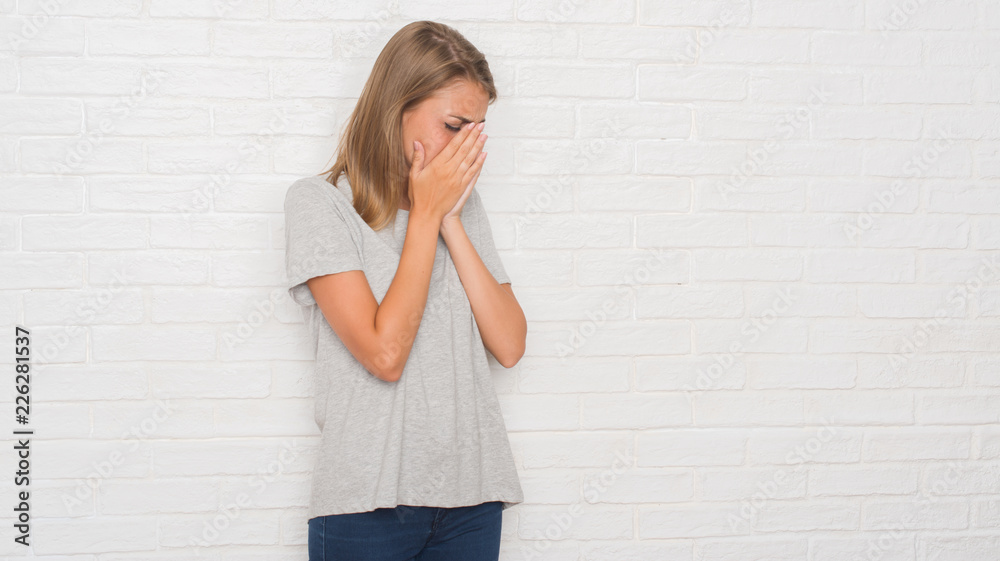 Beautiful young woman over white brick wall with sad expression covering face with hands while crying. Depression concept. Beautiful young woman over white brick wall with sad expression covering face with hands while crying. Depression concept.