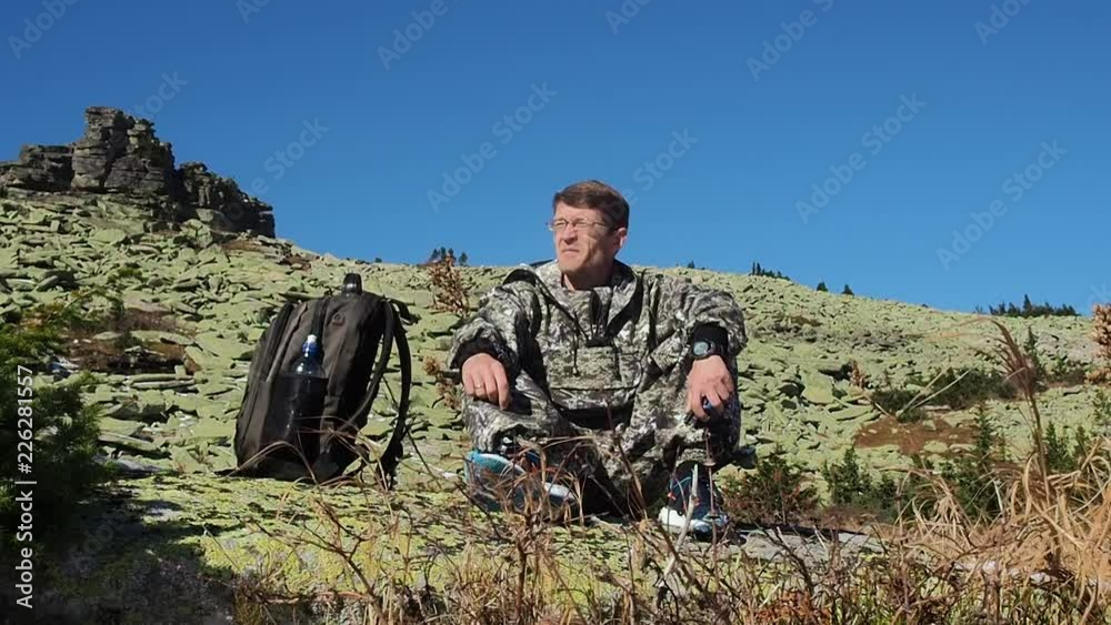 Male tourist sitting on a rock after a long walk on a mountain background. Male tourist sitting on a rock after a long walk on a mountain background.