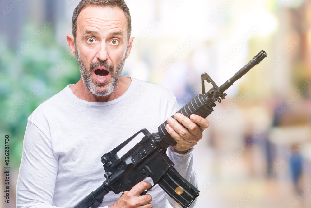 Middle age senior hoary criminal man holding gun weapon over isolated background scared in shock with a surprise face, afraid and excited with fear expression Middle age senior hoary criminal man holding gun weapon over isolated background scared in shock with a surprise face, afraid and excited with fear expression
