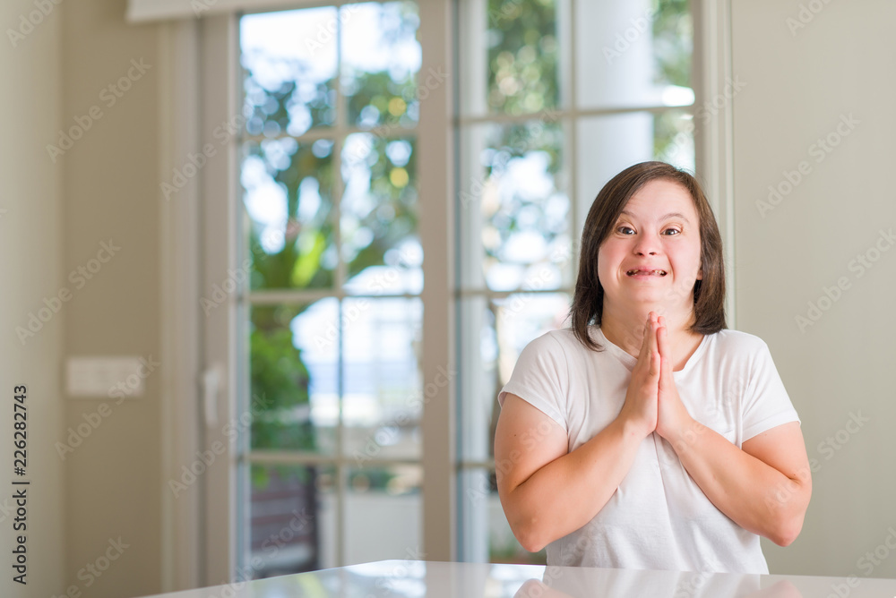 Down syndrome woman at home praying with hands together asking for forgiveness smiling confident. Down syndrome woman at home praying with hands together asking for forgiveness smiling confident.