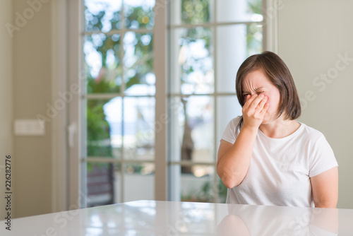 Down syndrome woman at home tired rubbing nose and eyes feeling fatigue and headache. Stress and frustration concept.