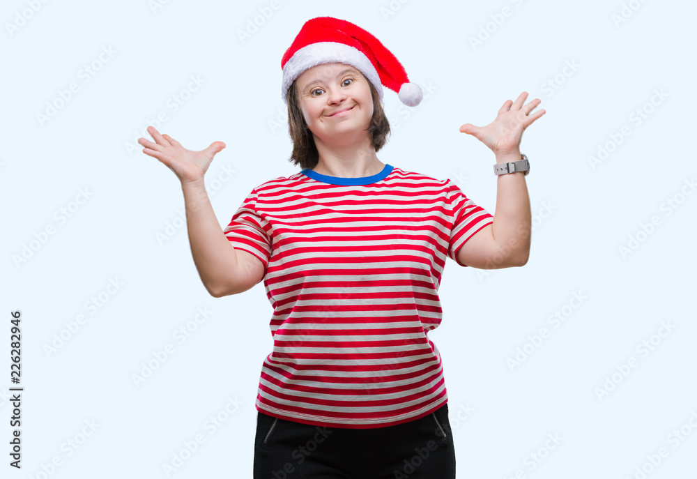 Young adult woman with down syndrome wearing christmas hat over isolated background crazy and mad shouting and yelling with aggressive expression and arms raised. Frustration concept. Young adult woman with down syndrome wearing christmas hat over isolated background crazy and mad shouting and yelling with aggressive expression and arms raised. Frustration concept.