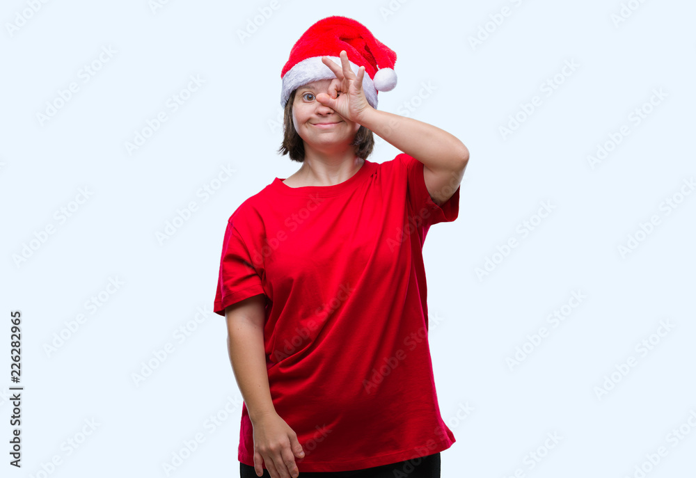 Young adult woman with down syndrome wearing christmas hat over isolated background doing ok gesture with hand smiling, eye looking through fingers with happy face. Young adult woman with down syndrome wearing christmas hat over isolated background doing ok gesture with hand smiling, eye looking through fingers with happy face.