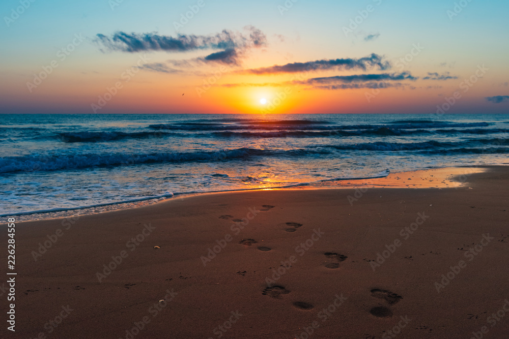 Amazing colorful sunrise at sea, footprints in the sand