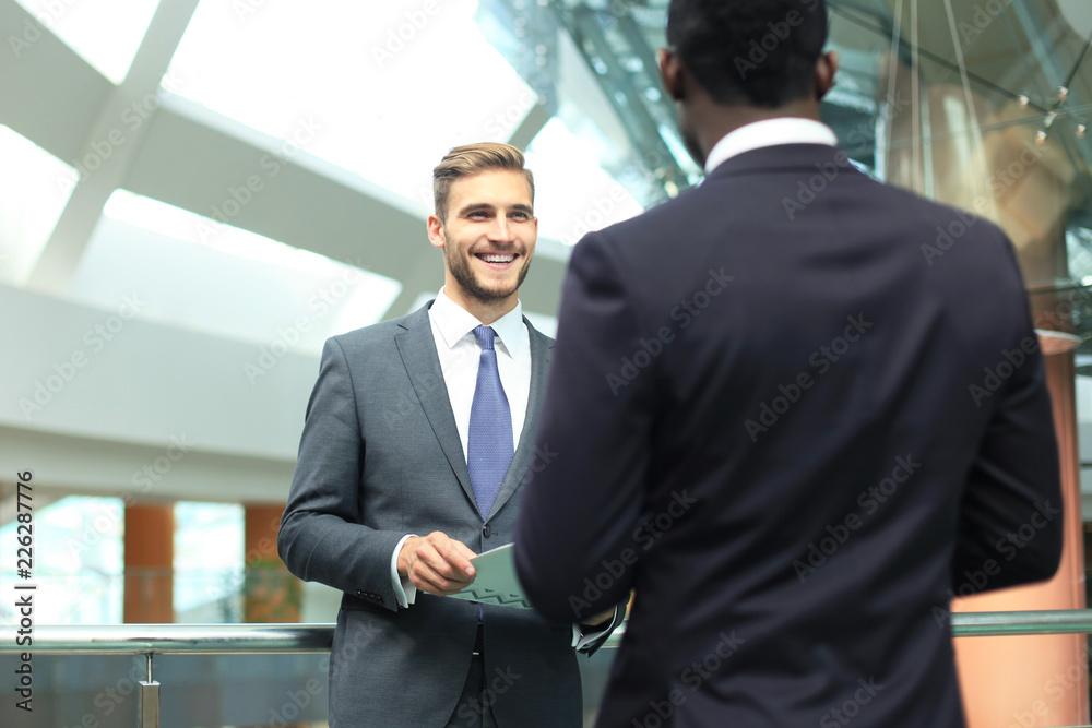 Two multinational young businessmen discussing business at meeting in office.
