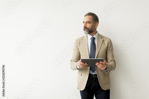 Handsome senior businessman with tablet by wall