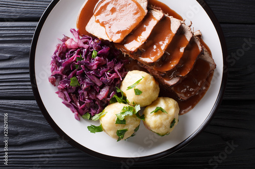 German roast pot Sauerbraten served with potato dumplings and red cabbage close-up. horizontal top view