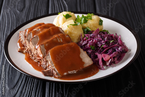 German food Sauerbraten - slowly stewed marinated beef with gravy with potato dumplings and red cabbage close-up on a plate. horizontal photo