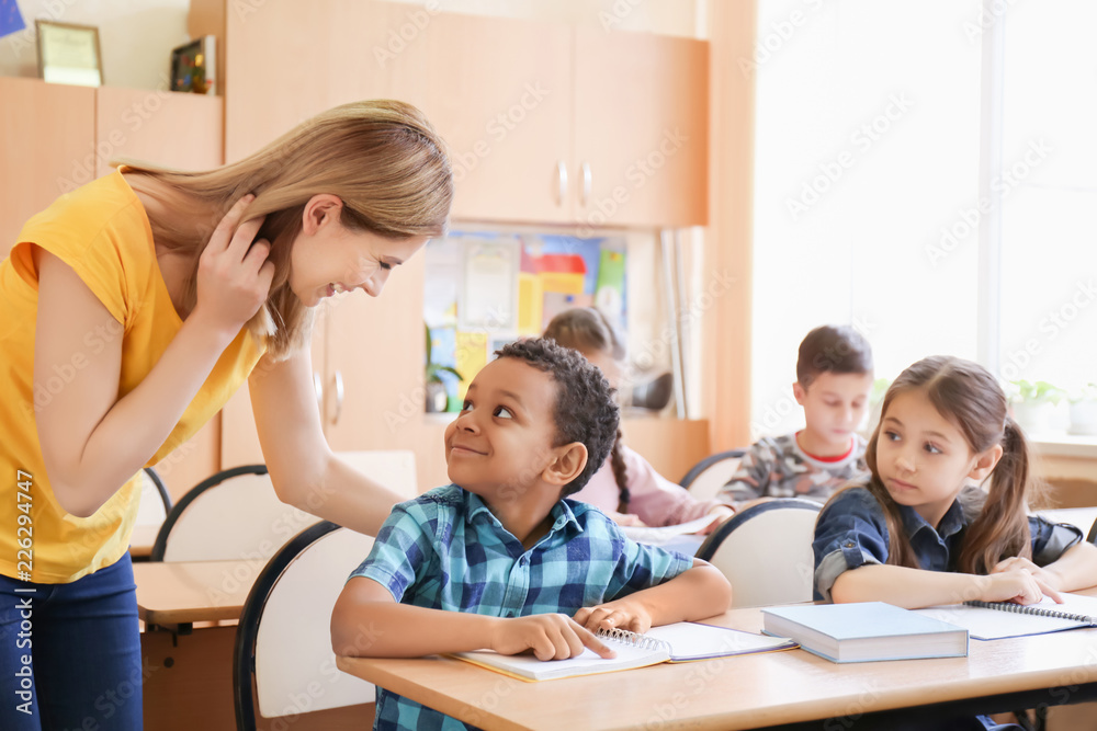Female teacher helping boy with his homework in classroom at school Female teacher helping boy with his homework in classroom at school