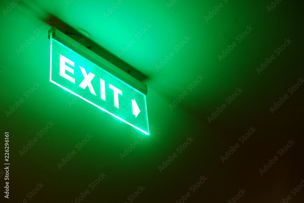 Perspective view of green emergency fire exit sign hanging on the ceiling Perspective view of green emergency fire exit sign hanging on the ceiling