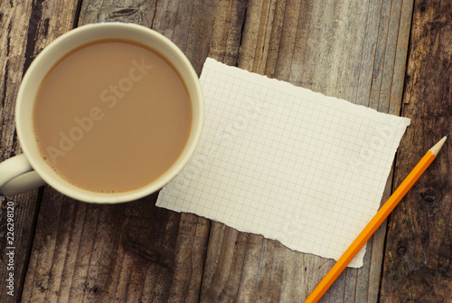 Empty blank page paper and cup of coffee on wooden table. Ready for adding text or mockup. Retro filtered. Flat lay.