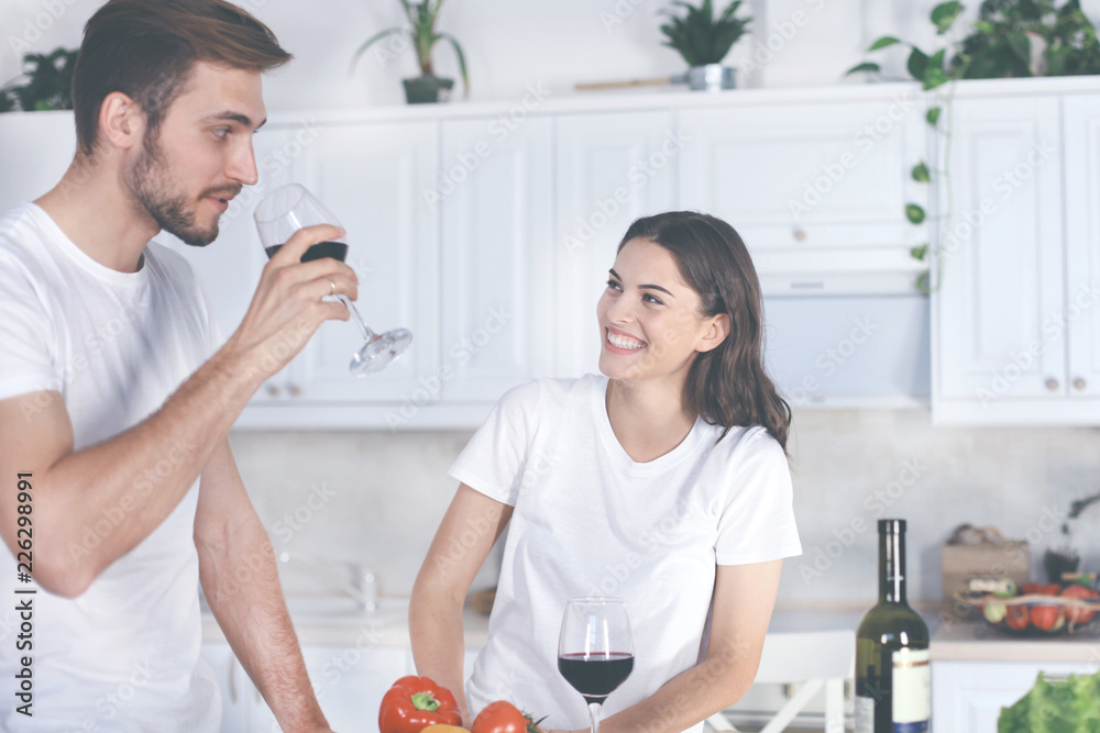 Beautiful young couple is drinking wine and smiling while cooking in kitchen at home. Beautiful young couple is drinking wine and smiling while cooking in kitchen at home.