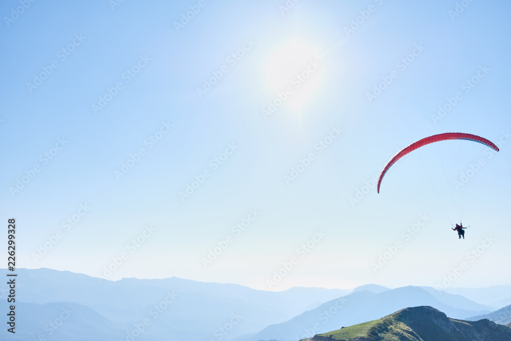 Parachute with one person glides across the clear sky over a beautiful mountain landscape. Non-urban scene. Travel destination. Sports activities Parachute with one person glides across the clear sky over a beautiful mountain landscape. Non-urban scene. Travel destination. Sports activities