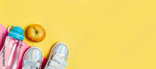 Child sneackers and bottle of water on yellow background.