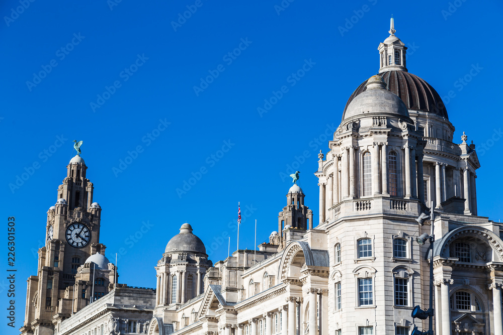 Obraz premium The three buildings (Port of Liverpool Building, Cunard Building and Royal Liver Building) which make up the Three Graces on the Liverpool waterfront under a blue sky.