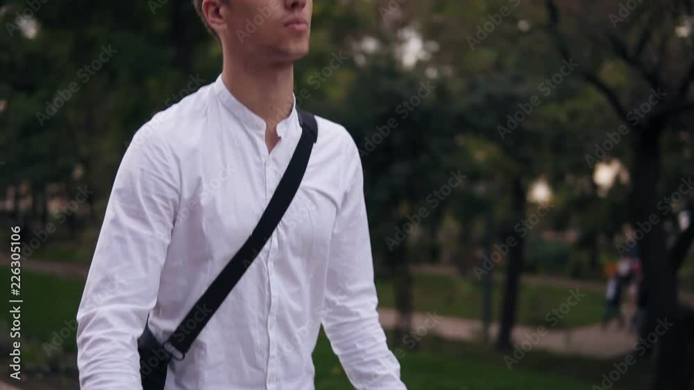 Caucasian young businessman walking with bicycle on the street in town. Rolling his trekking bike while walking by park with laptop case on shoulder. Slow motion Caucasian young businessman walking with bicycle on the street in town. Rolling his trekking bike while walking by park with laptop case on shoulder. Slow motion