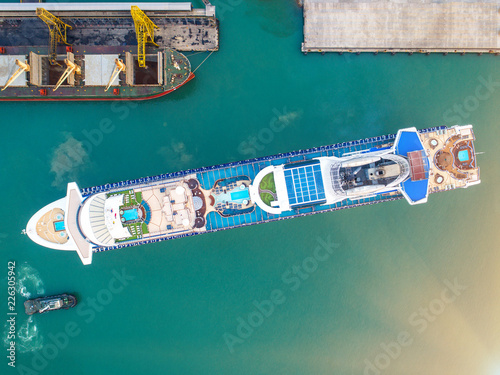 aerial top view of the passenger cruise vessel ship is in the port, arrival and departure of the ship under command and navigation by pilot and captain, withn tug boat assist for safety attending
