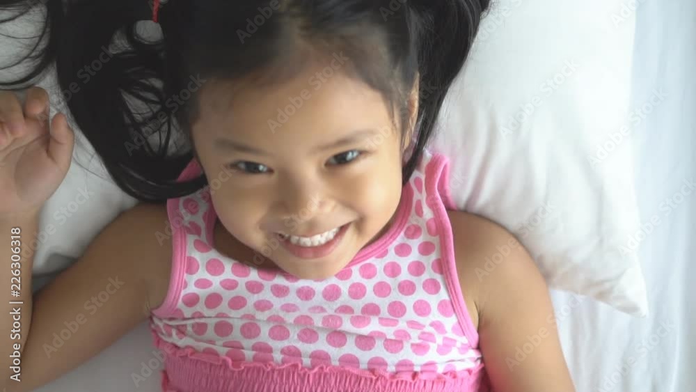 Asian child cheerful or kid girl sleeping and wake up for relax and playing together with father or mother on white bed and pillow in bedroom and smile laugh for enjoy happy fun in holiday morning