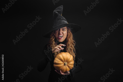 Halloween Witch with pumpkin. Pretty young woman in witch costume. Halloween decor. Copy space.