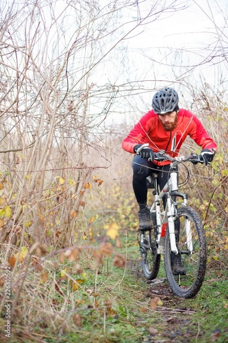 Determined young bearded man riding mountain bike through bushes on a cold foggy autumn or winter day