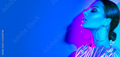 Fashion model brunette woman in colorful bright neon lights posing in studio. Beautiful sexy girl, trendy glowing makeup, metallic silver lips