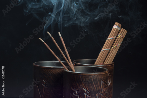 Burning incense sticks and brown bowl on black background. Beautiful smoke from above