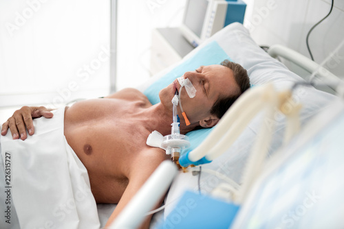 Stable condition. Side view portrait of patient on mechanical ventilator lying in bed under white sheets photo